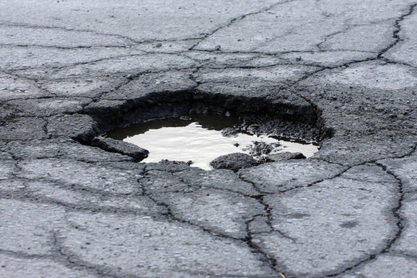 the pothole is a significant depression in the road surface, and it has collected rainwater or other liquid. The surrounding asphalt is severely cracked and deteriorated, indicating poor road conditions and the need for pavement repair. The presence of water in the pothole further exacerbates the damage by seeping into the cracks and weakening the road structure. This is a common road hazard that can affect vehicle safety and ride quality in areas with inadequate road maintenance.