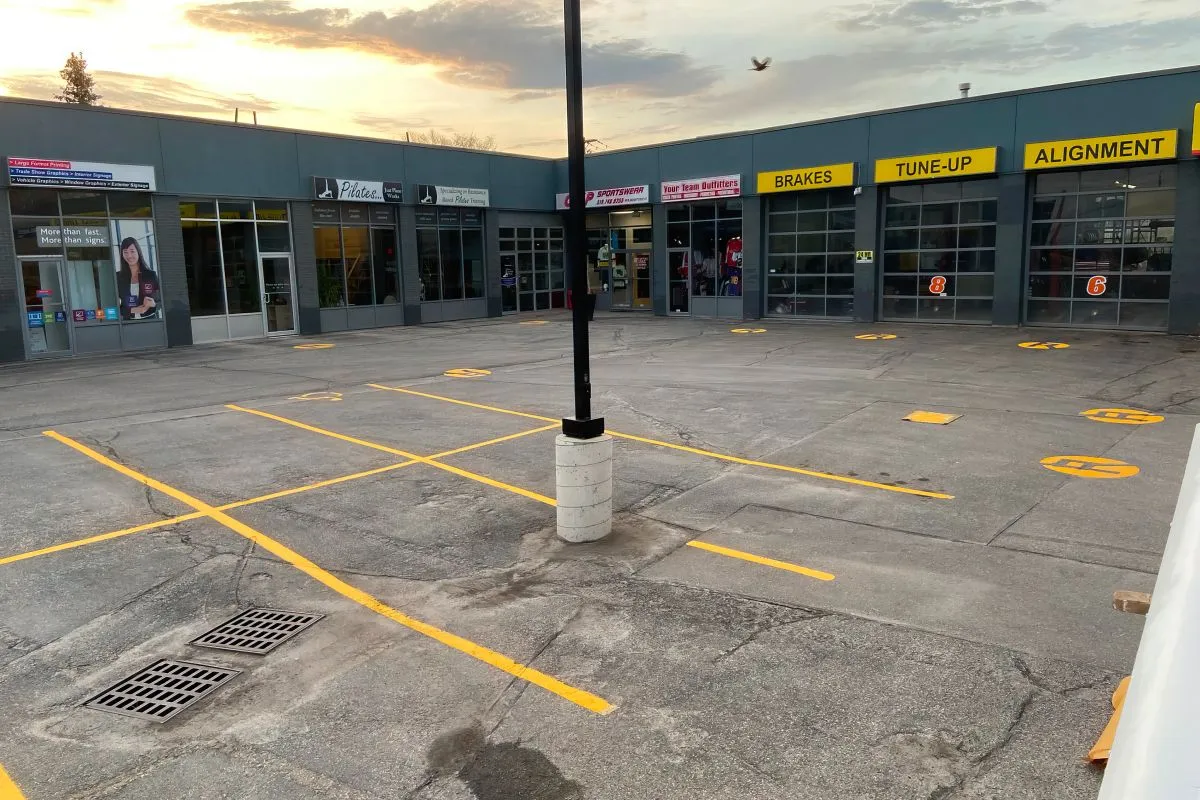 The image shows the exterior of a multi-bay automotive service center. The bays are labeled with yellow signs indicating the services offered: BRAKES, TUNE-UP, and ALIGNMENT. Each bay door has a large red number "8" or "6" painted on it.