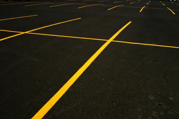 newly paved black asphalt. Bright yellow lines are freshly painted to delineate parking spaces. The lines are sharp and clearly visible against the dark, unmarked pavement, indicating recent pavement marking work.
